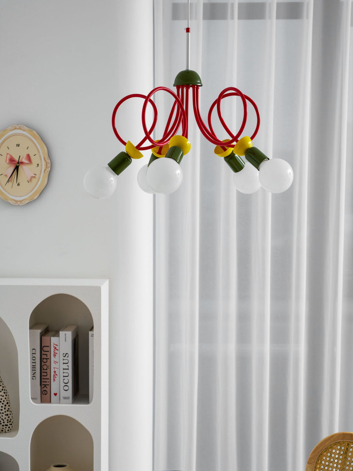 Cropped view of this Clérachic pendant's red loops and bulbs, with curtains and an arched bookshelf beside it.