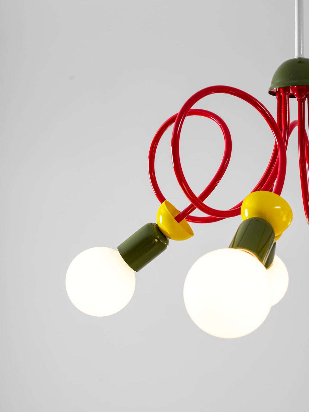 Detail of two globe bulbs, yellow collars and green sockets on this Clérachic pendant, with red tubes curling above.