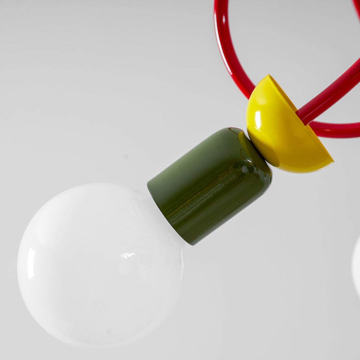 Close view of one green socket with a yellow collar, a red tube and a frosted globe bulb on this Clérachic pendant.