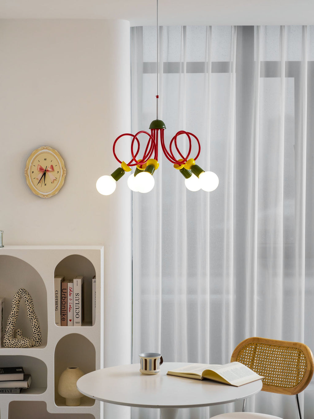 Clérachic pendant with its bulbs lit above a round white table, with an open book, a mug and an arched shelf behind.
