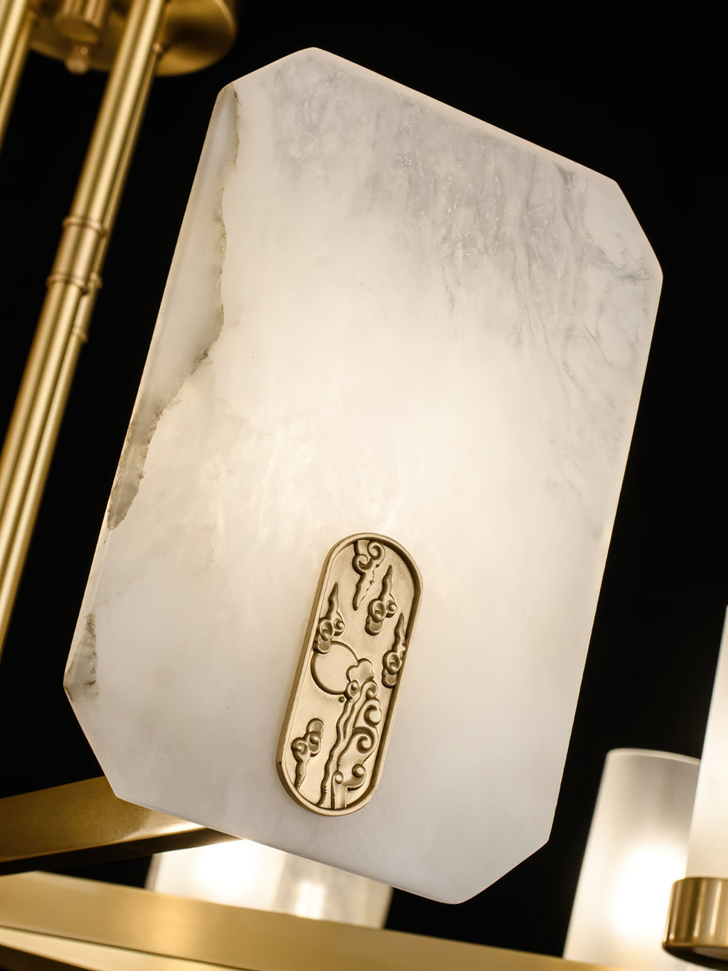 Detail of the Clérachic Meridian Alabaster Chandelier: lit alabaster glowing warm around a raised brass cloud motif plaque.