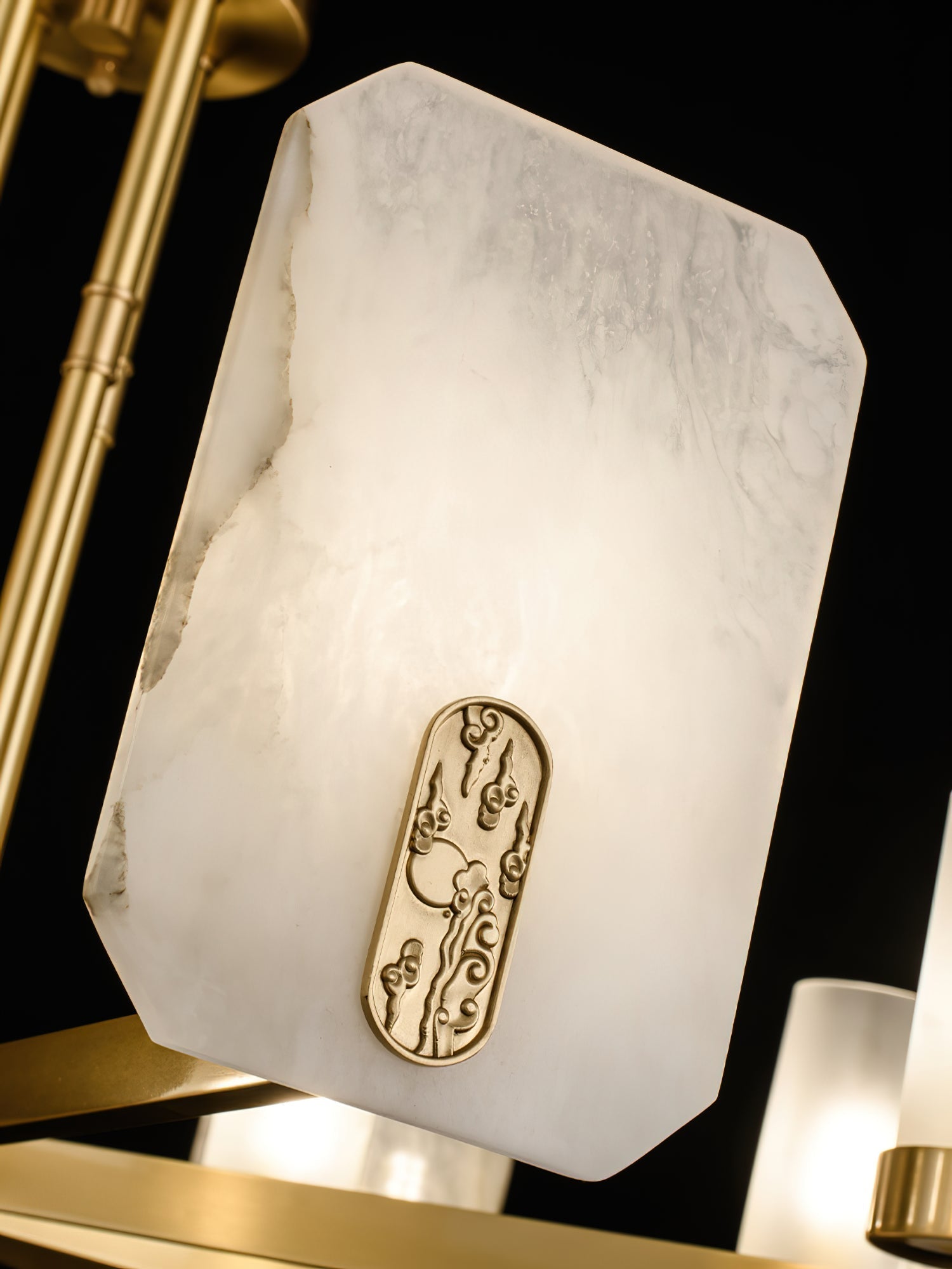 Detail of the Clérachic Meridian Alabaster Chandelier: lit alabaster glowing warm around a raised brass cloud motif plaque.