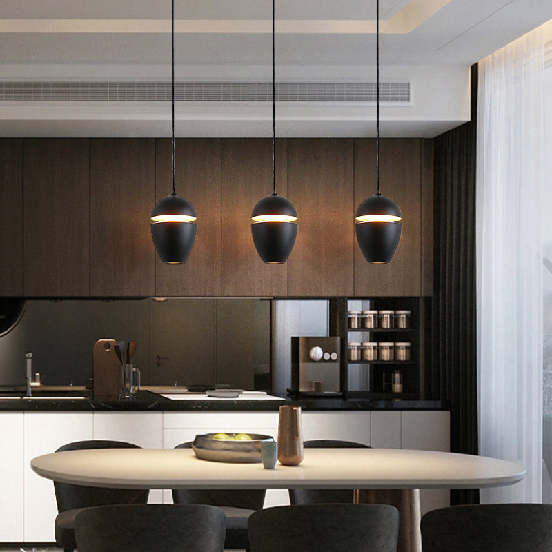 Clérachic matte black acorn pendants hang in a row over an oval dining table, each with a warm glowing slit.