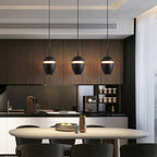 Clérachic matte black acorn pendants hang in a row over an oval dining table, each with a warm glowing slit.