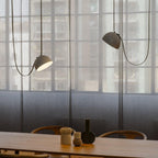 Two Clérachic pendant lights with grey domes hang on dark cords in front of a tall gridded window, above a long wooden dining table.
