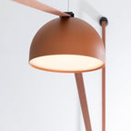 Close view from below of an orange metal dome on this Clérachic pendant light, with its flat red fabric strap running across a white wall.