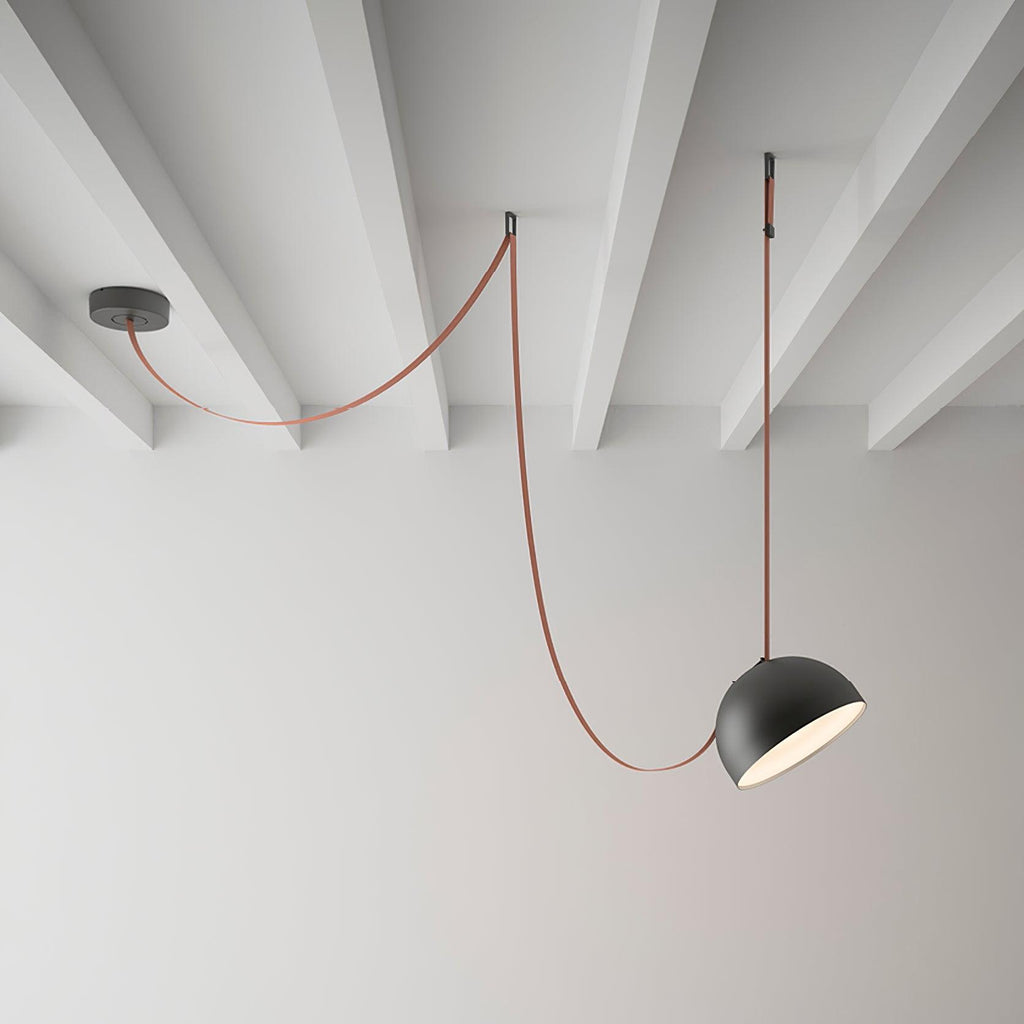 A black dome on this Clérachic pendant light hangs from a red fabric strap looped from a ceiling plate across a white beamed ceiling.