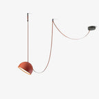Mirrored view of this Clérachic pendant light, with an orange dome on the left and the red strap looping up to a dark ceiling plate on the right.