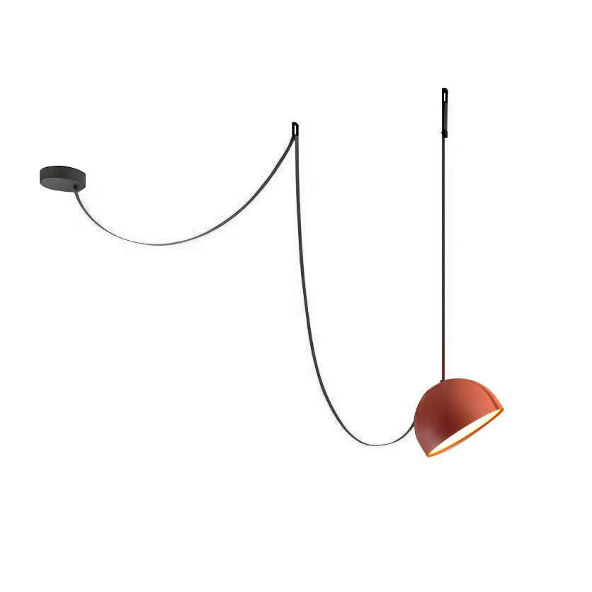 This Clérachic pendant light on a white backdrop, with an orange dome hanging from a black strap looped over a ceiling plate.