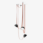 Three black-domed Clérachic pendant lights hang at different heights from red woven straps, on a pale grey studio backdrop.