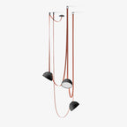 Another view of the three-head Clérachic pendant light with black domes and red woven straps, one shade turned to show its glowing underside.