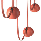 Close view of three orange domes on this Clérachic pendant light, each held by a woven red strap through a small black buckle.
