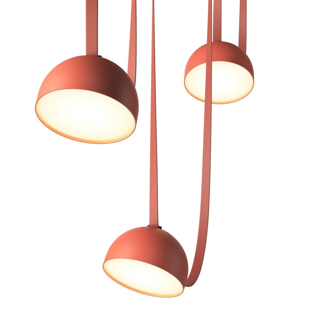 Looking up at three orange domes of this Clérachic pendant light, their warm white interiors glowing, with red straps hanging between.