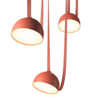Looking up at three orange domes of this Clérachic pendant light, their warm white interiors glowing, with red straps hanging between.