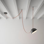 A black-domed Clérachic pendant light hangs on a red fabric strap in a bare white room with exposed beams and a grey wall.