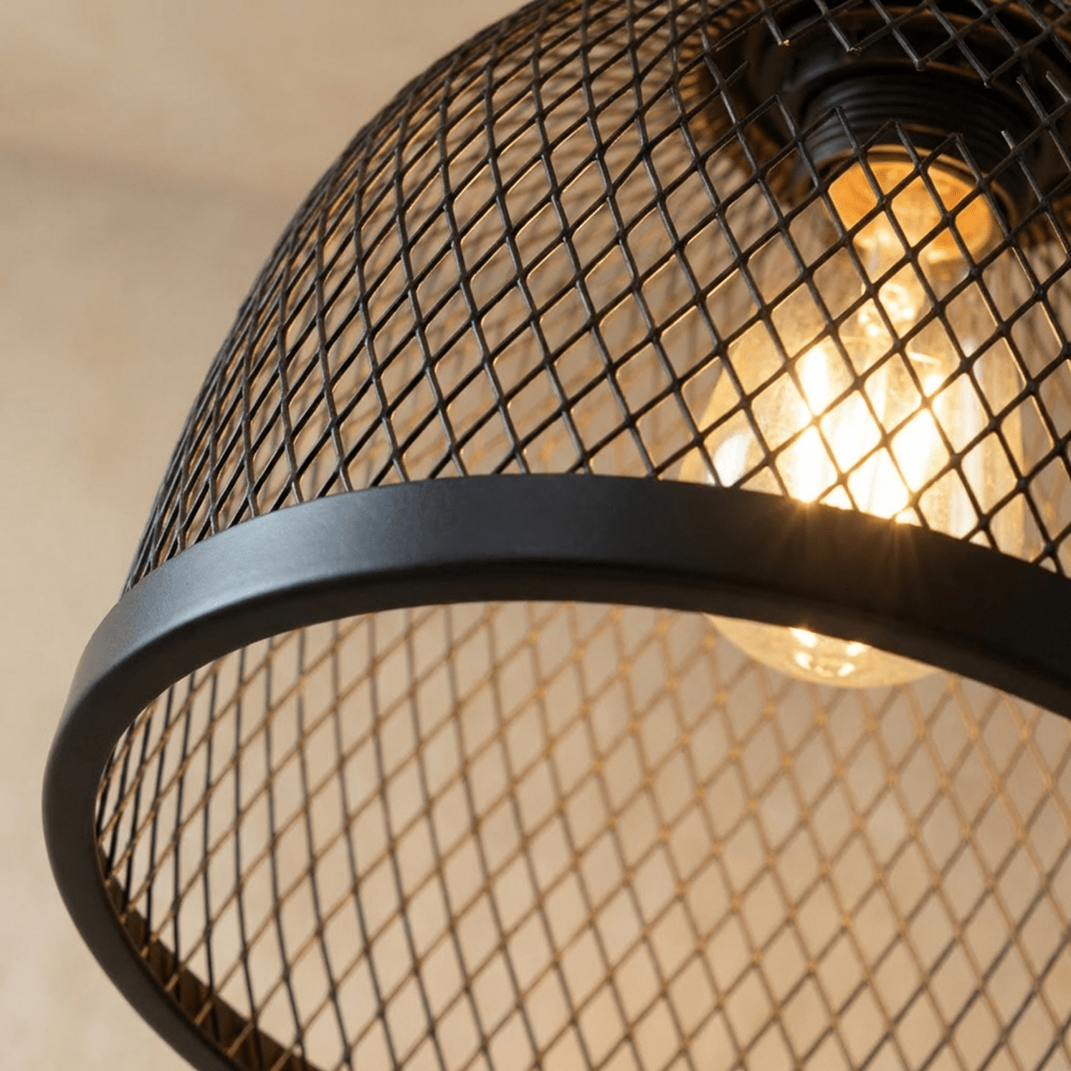 Close view of the black wire-mesh dome and matte rim on a Clérachic pendant, with a warm bulb glowing through