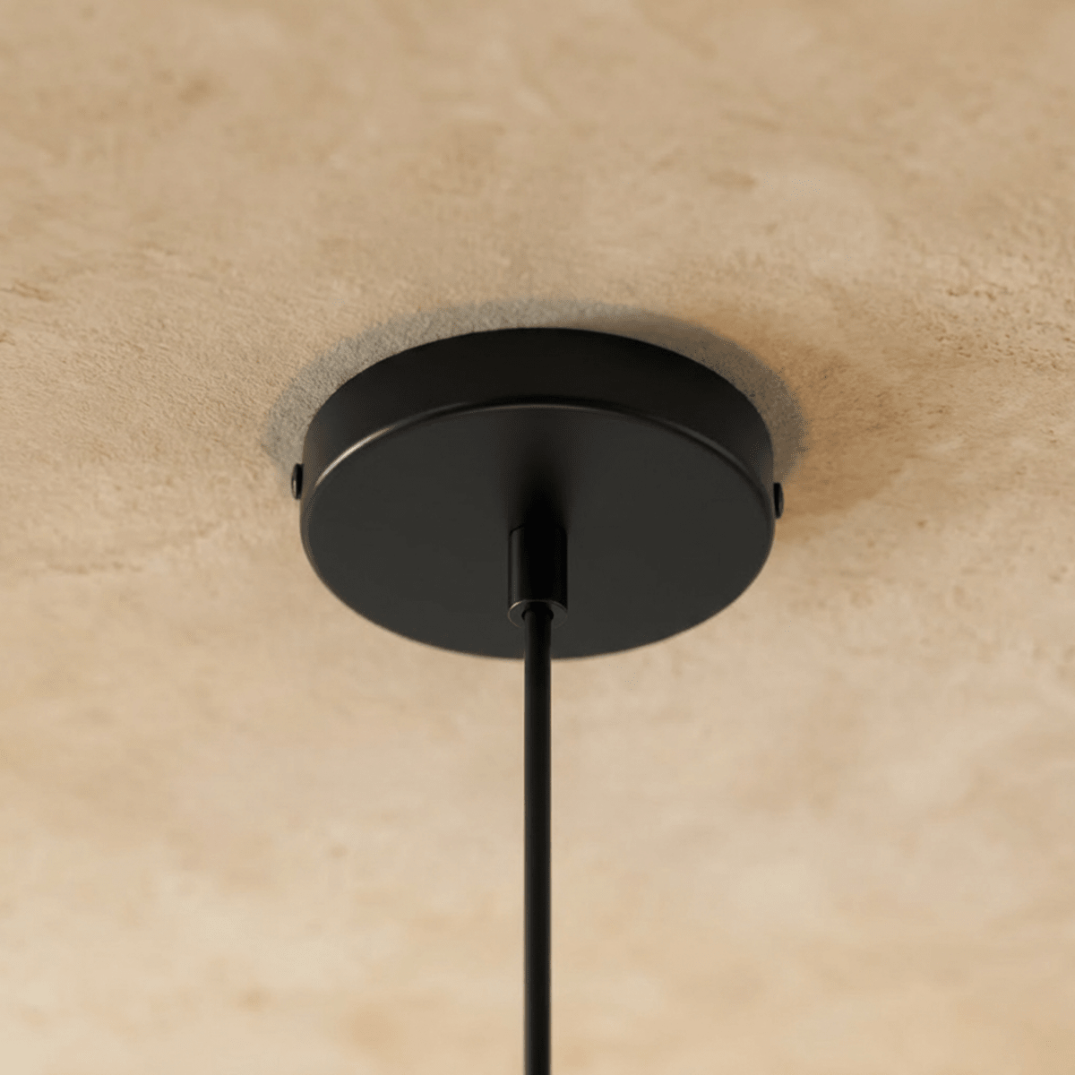 Underside of the matte black round ceiling canopy on a Clérachic pendant, with the black cord leaving its centre