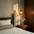 Clérachic domed mesh pendant glowing beside a bed with linen bedding, a walnut nightstand and a concrete wall