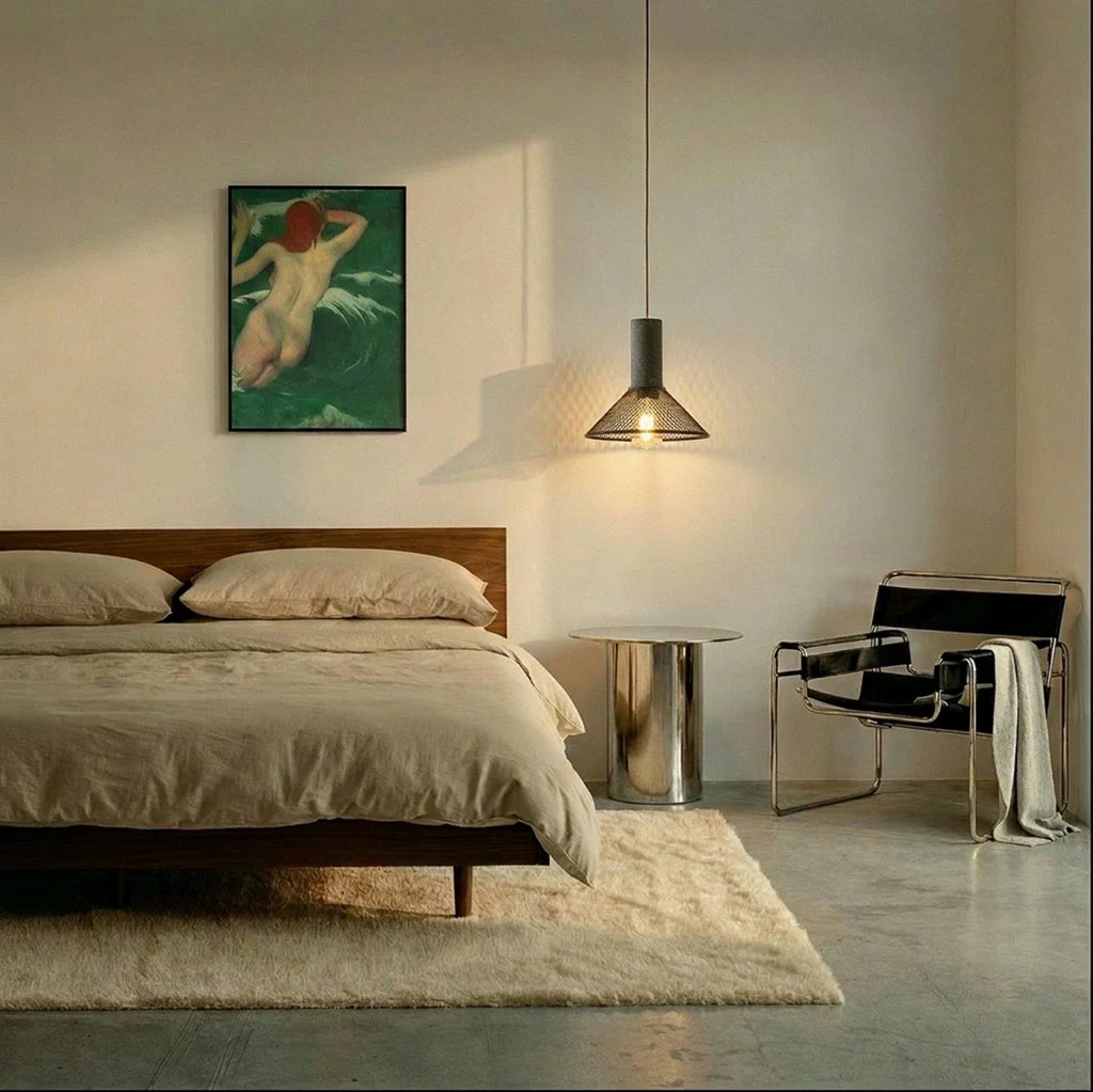 Clérachic conical mesh pendant glowing beside a walnut bed, with a steel side table and a leather chair
