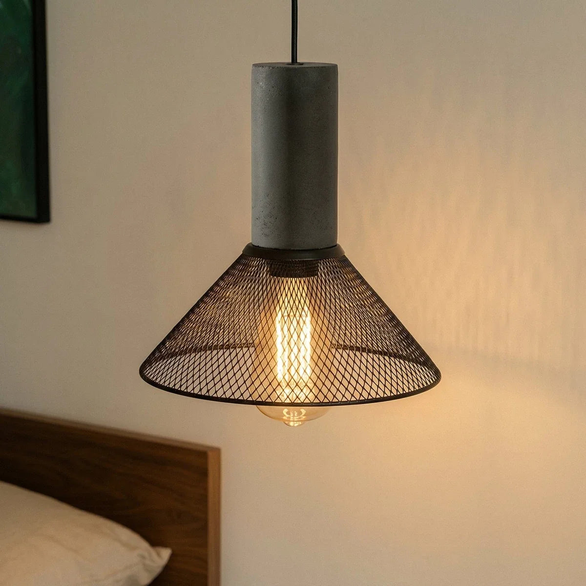 Close view of a Clérachic conical mesh pendant, its grey cylindrical collar and warm globe bulb lit by the bed