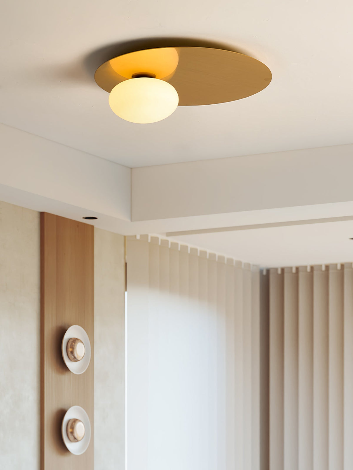 Brass Clérachic ceiling light lit beside a ceiling recess, with pleated curtains and a wood panel in the background.