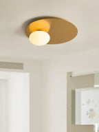 Lit brass Clérachic ceiling light with a glass globe, seen from below in a bright room with a slatted blind.