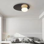 Black Clérachic ceiling light with a glowing glass globe above a plain white bedroom lit by streaks of sunlight.