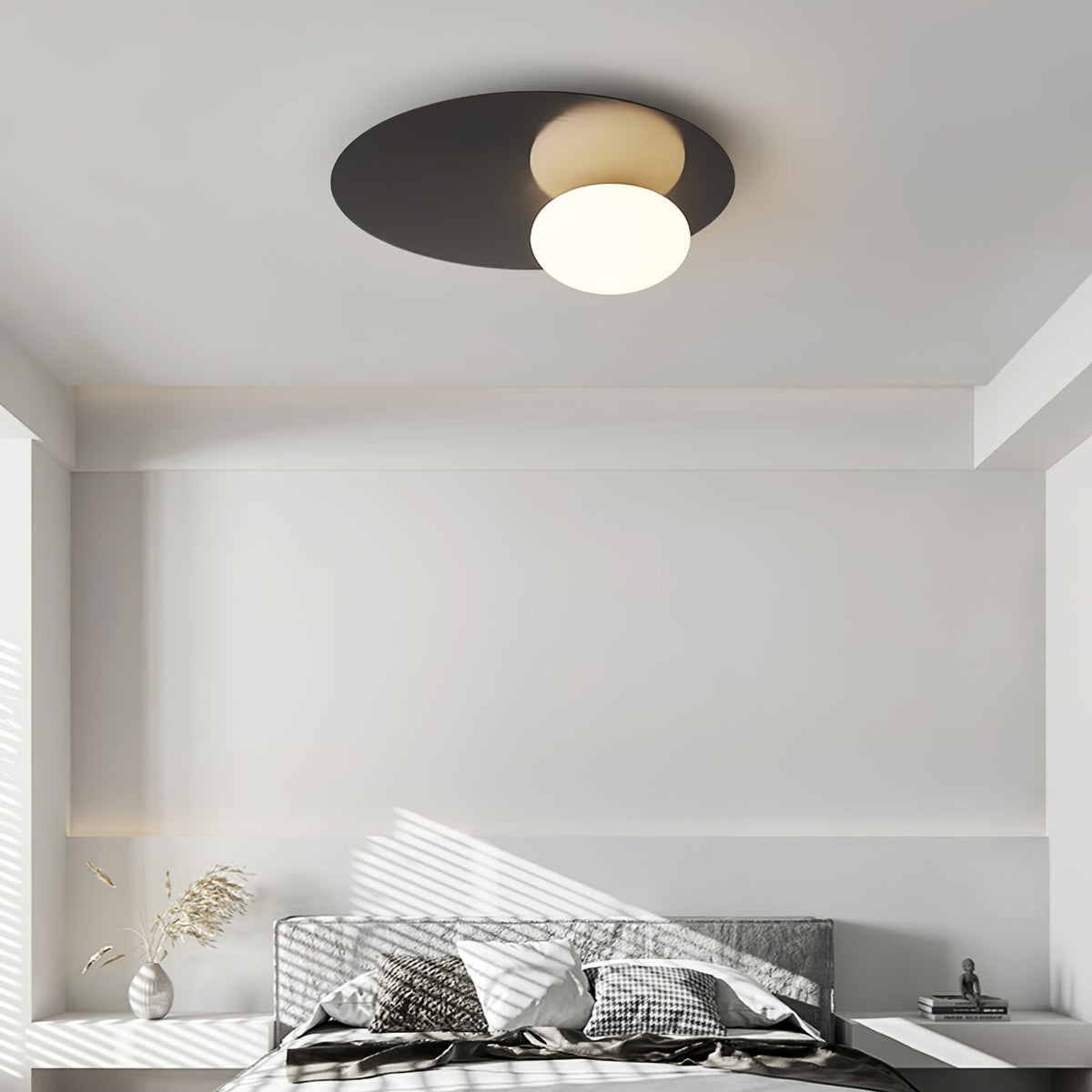Black Clérachic ceiling light with a glowing glass globe above a plain white bedroom lit by streaks of sunlight.