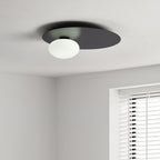 Black Clérachic disc ceiling light with an unlit white glass globe, seen at the corner of a room near a window blind.