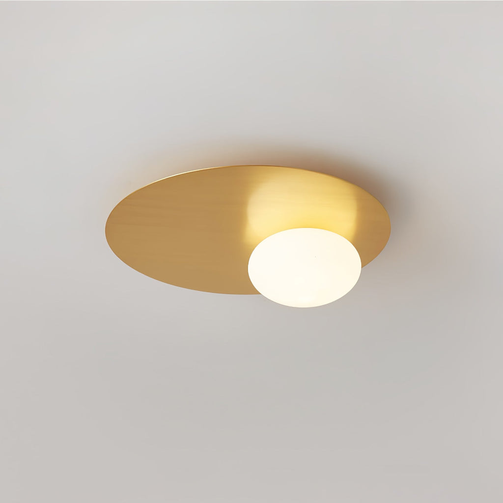 Brass Clérachic ceiling light with a glowing white globe, shown close on a smooth pale ceiling.