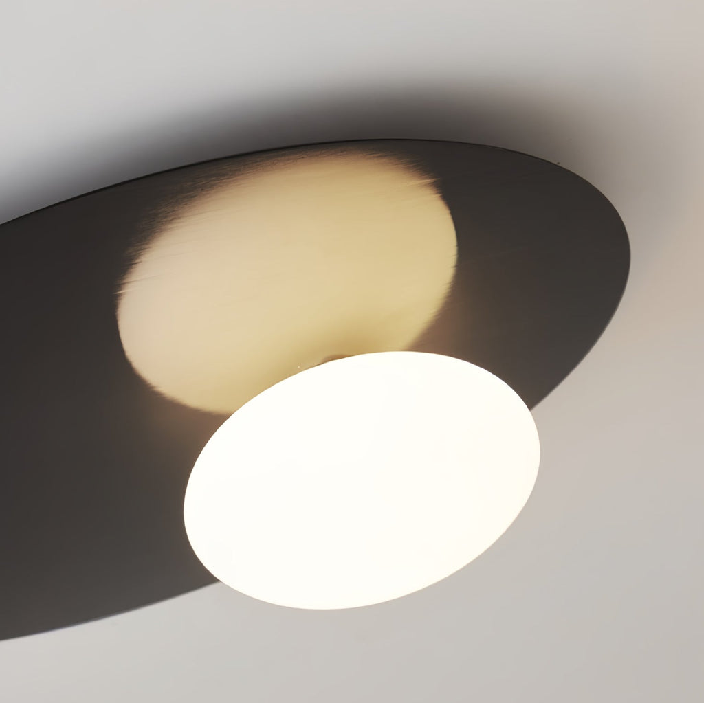 Close view from below of the lit milk glass globe and dark metal disc on this black Clérachic ceiling light.