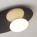 Close view from below of the lit milk glass globe and dark metal disc on this black Clérachic ceiling light.