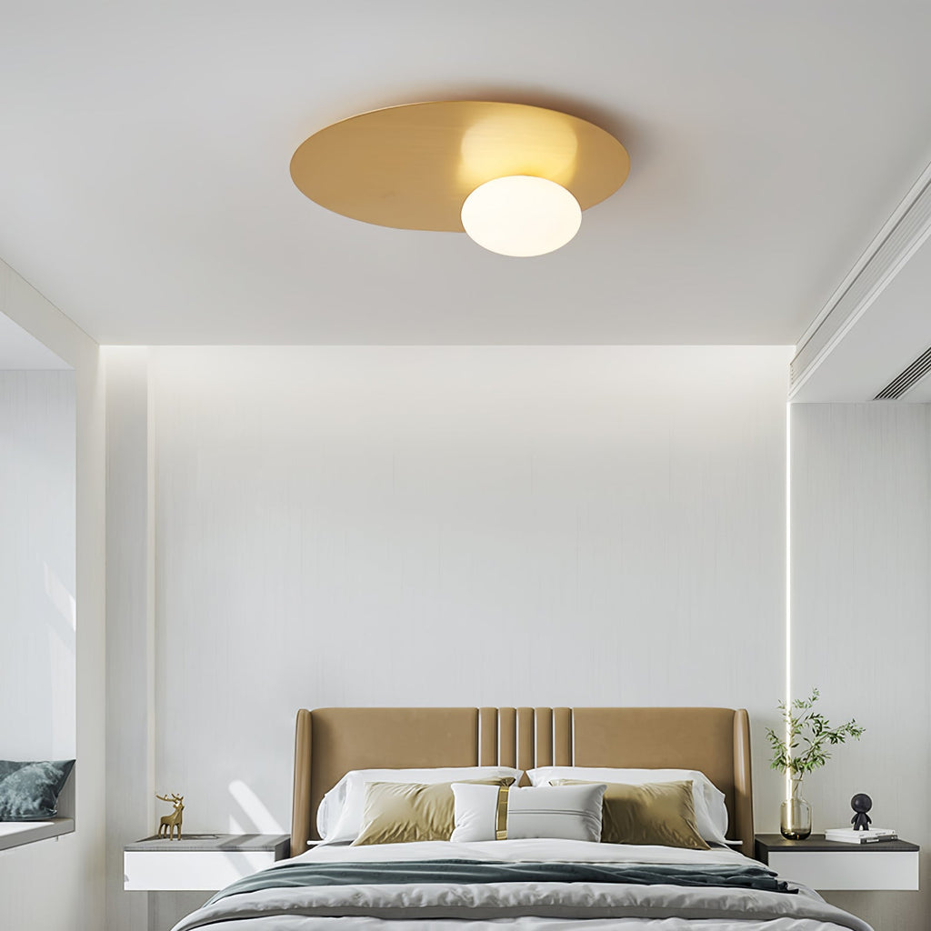 Brass Clérachic ceiling light with a white globe above a calm bedroom with a tan upholstered headboard and wall lighting.