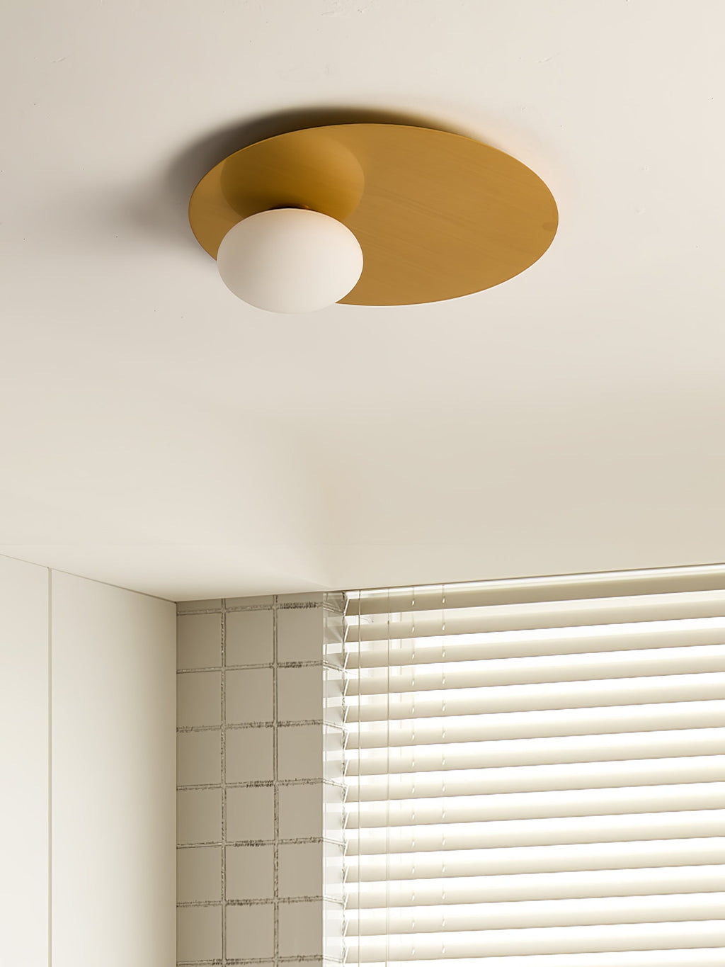 Brass Clérachic ceiling light with an opal glass globe in a cream room beside a window with a horizontal blind.