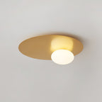 Wide brass Clérachic disc with a white glass globe fixed to a pale ceiling, with the oval shape clearly visible.