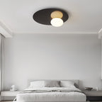 Black Clérachic disc ceiling light with a lit globe above a neatly made bed in a quiet grey bedroom.