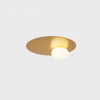 Brass Clérachic ceiling light lit on a light grey background, its globe set off-centre on the disc.