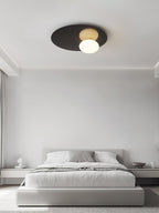 Black Clérachic ceiling light above a bed with grey linen in a bright room with a soft curtain at the side.