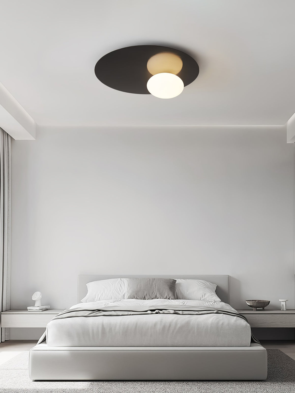 Black Clérachic ceiling light above a bed with grey linen in a bright room with a soft curtain at the side.