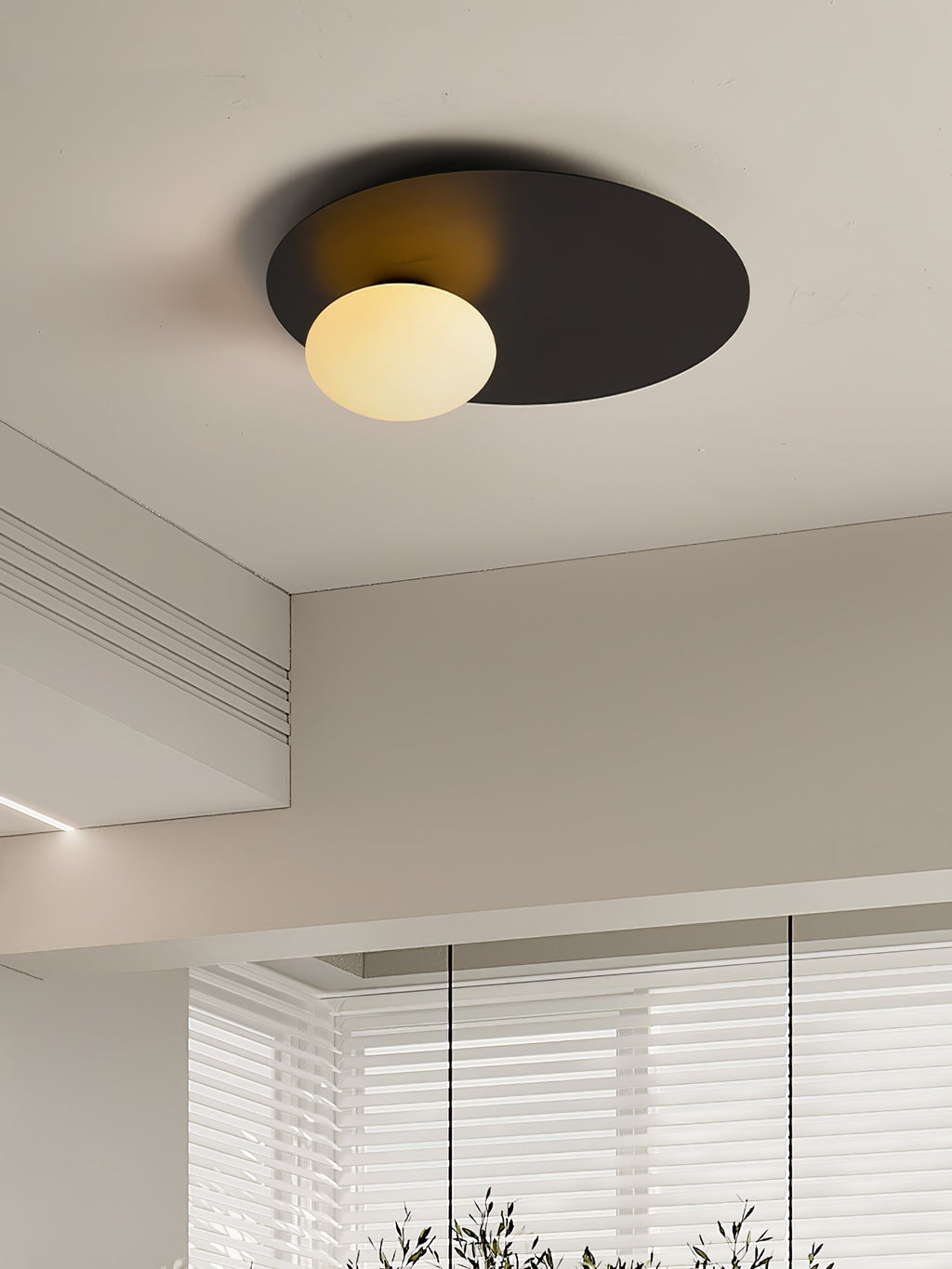 Black Clérachic ceiling light with a warm-lit globe in a beige room with a deep ceiling coffer and a slatted blind.
