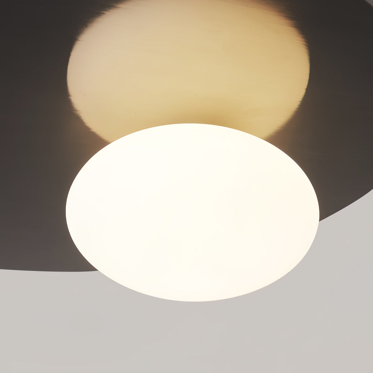 Close view of the milk glass globe lit warm against the dark metal disc of this Clérachic ceiling light.
