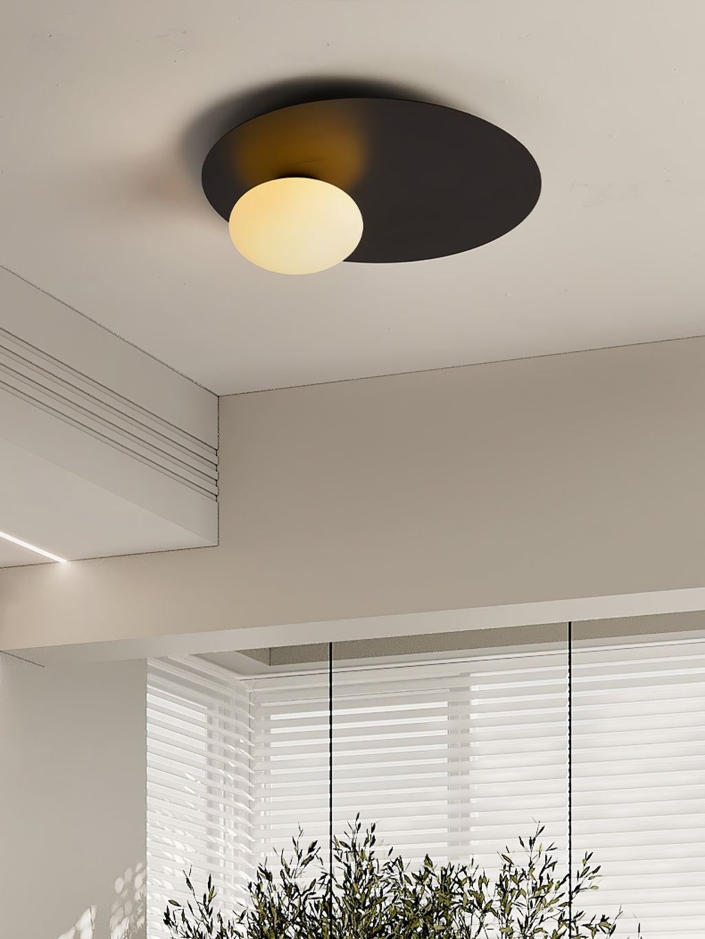 Lower view of the black Clérachic ceiling light lit in a beige room with a coffered ceiling and a window blind.