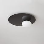 Black Clérachic ceiling light unlit, with a white glass globe against the dark disc on a light ceiling.