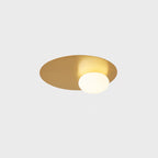 Brass Clérachic ceiling light lit on a pale grey backdrop, with the white globe glowing against the brushed disc.
