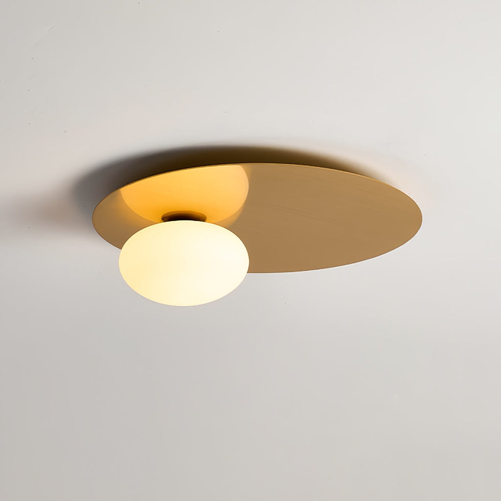 Brass Clérachic ceiling light lit, its brushed disc catching a warm glow from the globe in a soft-lit room.