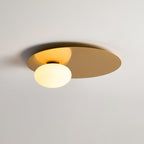 Brass Clérachic ceiling light lit, its brushed disc catching a warm glow from the globe in a soft-lit room.