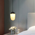 Clérachic milk glass pendant light in its stepped Art Deco shade, hung low beside a bed over a nightstand of white tulips.