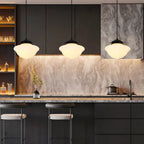 Three Clérachic milk glass pendant lights with wide schoolhouse dome shades lit in a row above a dark kitchen island.