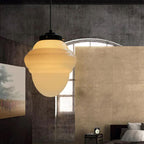 Clérachic milk glass pendant light in its rounded acorn profile, glowing against a raw concrete wall in a loft bedroom.