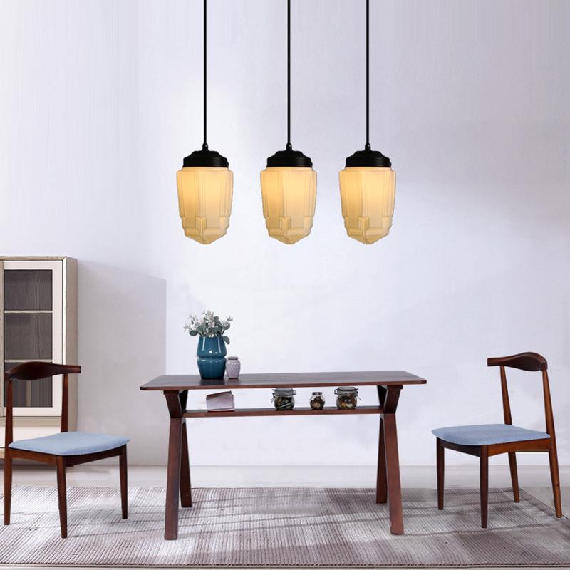 Three Clérachic milk glass pendant lights in the faceted cylinder shade, hung in a row above a dark wood dining table.